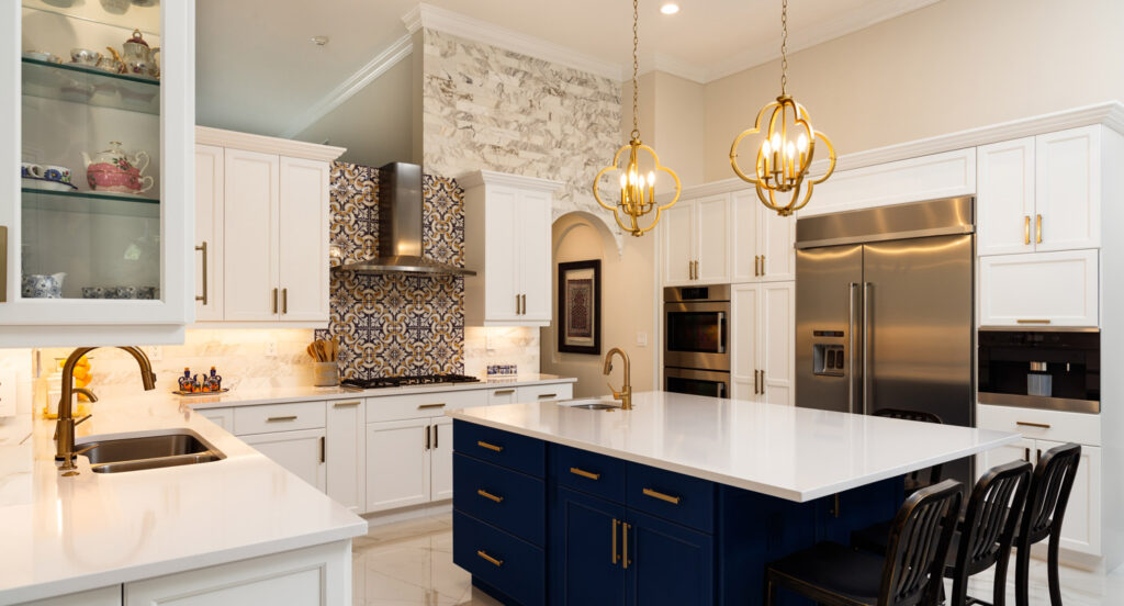 Modern kitchen with white cabinets, blue island, gold hardware, stainless steel appliances, patterned tile backsplash, and two pendant lights over the island.
