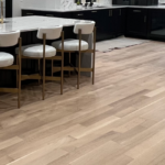 Modern kitchen with light wood flooring, a large island with four white and gold barstools, and black and white cabinetry.